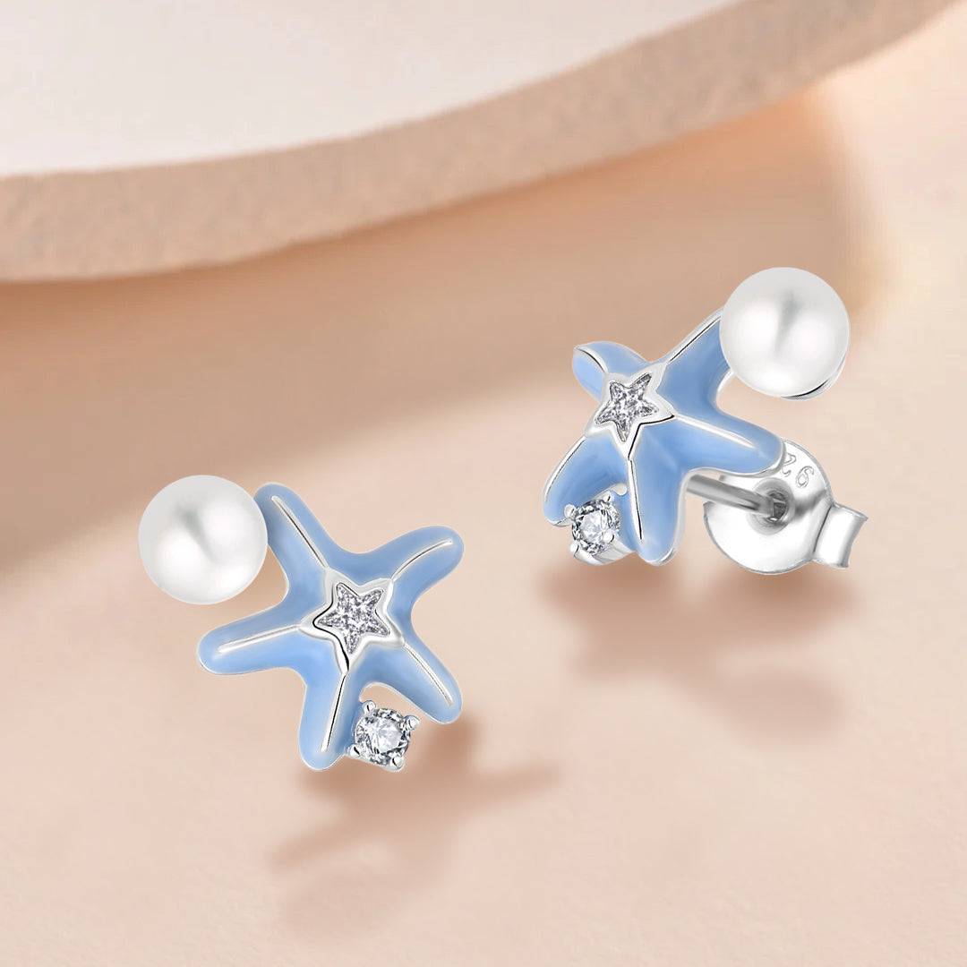 Starfish-shaped earrings with blue accents and clear gemstones on a beige background